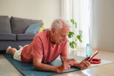 Son sınıf öğrencisi yoga minderine uzanmış akıllı telefon uygulaması kullanarak ev sporu egzersizleri yapıyor.