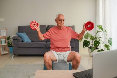 Gülümseyen son sınıf öğrencisi dizüstü bilgisayardaki beden eğitimi dersinden sonra evde dambıllarla egzersiz yapıyor.