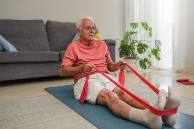 Evde kırmızı direniş bandıyla paspasın üzerinde egzersiz yapan kıdemli bir adam.