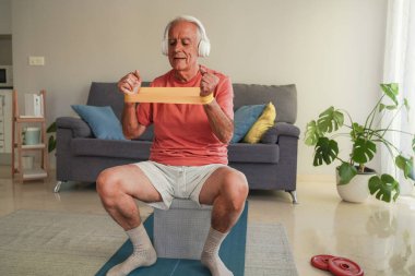 Evde direniş bandıyla egzersiz yaparken kulaklıkla müzik dinleyen son sınıf öğrencisi.