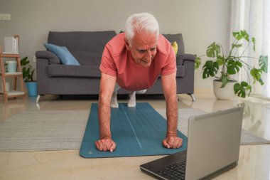 Son sınıf öğrencisi yoga minderinde şınav çekiyor evde dizüstü bilgisayarda beden eğitimi dersini takip ediyor.