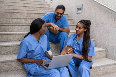 Çok ırklı tıp öğrencileri üniversite basamaklarında birlikte çalışıyor. Laptop kullanarak kahvenin tadını çıkarıyorlar.