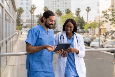 İki farklı çok ırklı sağlık çalışanı dışarıda dijital tablet üzerinde tıbbi bilgileri gözden geçiriyorlar.