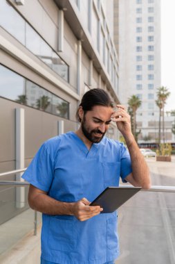 Endişeli doktor dijital tableti inceliyor ve hastane dışında stresli hissediyor.
