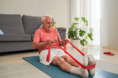 Emeklilik döneminde evde elastik bant, sağlık ve aktif yaşam tarzıyla egzersiz yapan yaşlı bir adam