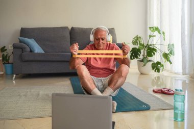 Son sınıf öğrencisi evde direniş bandıyla egzersiz yapıyor. Dizüstü bilgisayardan eğitim dersleri videosu izliyor.