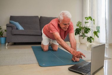 Dizüstü bilgisayardaki beden eğitimi dersinin ardından evde egzersiz yapan yaşlı bir adam.