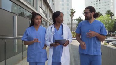 Hastane dışında yürürken hasta verilerini tabletten tartışan üniformalı tıbbi ekibin videosu.