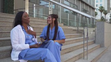Hastanenin merdivenlerinde dijital tablet kullanan iki çok ırklı kadın doktorun videosu.