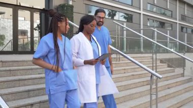 Hastanenin merdivenlerinden inip hasta bilgilerini tartışan tıbbi çok ırklı ekip videosu.