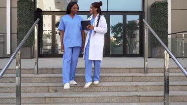 İki kadın doktor ve hemşirenin dijital masayı kullanarak hastanenin merdivenlerinden inerken videosu.