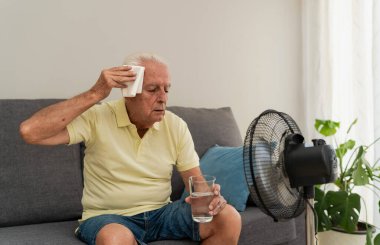 Suni teneffüs makinesinin yanında bir bardak su tutarken alnından ter siliyor.