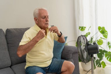 Evdeki yaz sıcağında koltukta oturmuş elektrikli vantilatörle serinliyor.