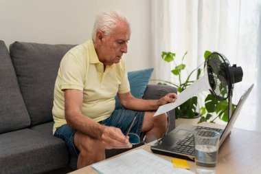 Son sınıf öğrencisi kanepede oturuyor ve yaz sıcağında ev ekonomisi ve elektrik faturalarını yönetiyor.