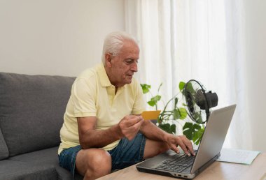 Üst düzey adam evdeki kanepede oturan dizüstü bilgisayarla ve kredi kartıyla online ödeme yapıyor.