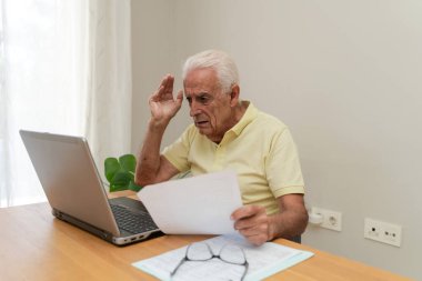 Evrak işlerini anlamakta zorlanan emekli bir adam evde dizüstü bilgisayarıyla uğraşırken endişeli.