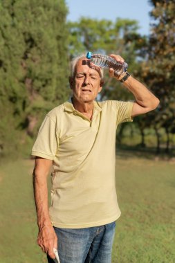 Kıdemli adam yaz sıcağında alnında su şişesiyle serinliyor.