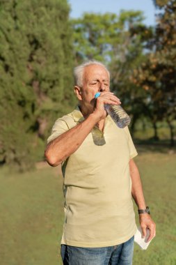 Kıdemli adam sıcak bir yaz günü parkta bir şişeden su içiyor.