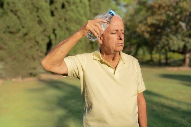 Son sınıf öğrencisi sıcak bir yaz gününde parkta su şişesiyle serinliyor.