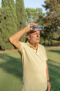 Kıdemli adamın yaz sıcağında alnında su şişesiyle serinlerken dikey görüntüsü.