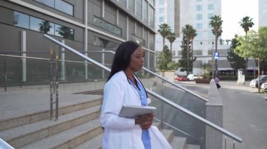 Kendine güvenen Afrikalı Amerikalı bir doktorun hastane merdivenlerinden inerken videosu.