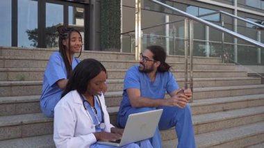 Çok ırklı doktorlar ve hemşirelerin basamaklarda oturup hasta vakalarını tartıştıkları video.