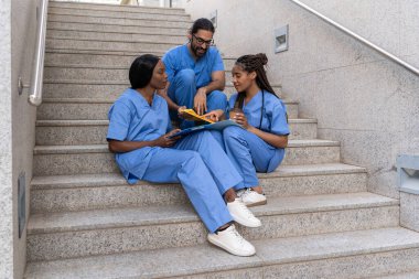 Tıbbi çeşitlilik hastane merdivenlerinde otururken hasta bilgilerini tartışıyor.