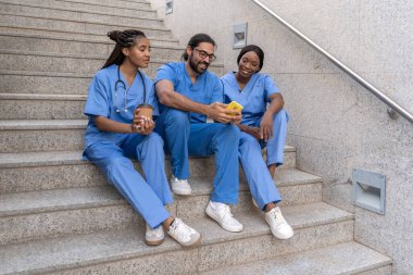 Doktorlar ve hemşireler hastane merdivenlerinde oturup kahve içiyorlar.