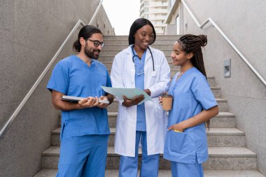 Çeşitli doktor ve hemşireler hastane merdivenlerindeki tıbbi kayıtları inceliyor.