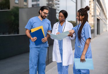 Dışarıdaki belgeleri inceleyen üniformalı çok ırklı sağlık uzmanları.