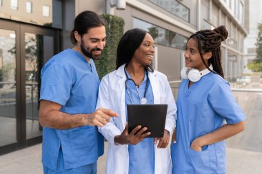 Çok ırklı doktorlar ve hemşireler tablet kullanıyorlar ve hasta bilgilerini hastane dışında tartışıyorlar.