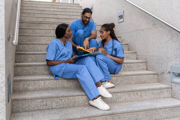 Tıbbi çeşitlilik hastane merdivenlerinde otururken hasta bilgilerini tartışıyor.