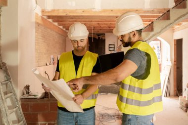 Bina planlarını inceleyen iki erkek inşaat işçisi ev inşaatında tadilat yapmayı planlıyor.