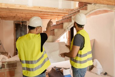 İki erkek inşaat işçisi planı inceliyor ve ev yenileme projesini tartışıyorlar.