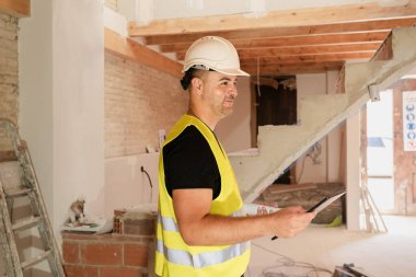 Ev tadilatı sırasında dijital tablet üzerindeki kontrol listesini kullanarak erkek denetleyici inşaat alanını kontrol ediyor