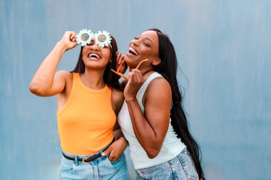 Mavi arka planda komik güneş gözlüğü takıp gülüp eğlenen iki bayan arkadaş.