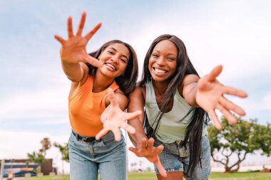 İki mutlu çok ırklı kadın dışarıda eğleniyor ve kameraya gülümsüyor.