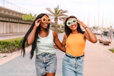 Komik güneş gözlüklü iki mutlu kadın yaz tatili boyunca turist limanında yürüyorlar.