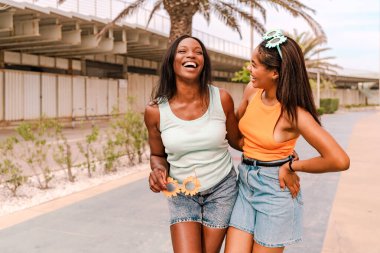 İki neşeli çok ırklı kadın bir yaz günü birlikte yürüyüp gülerek tatilin tadını çıkarıyorlar.