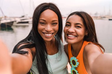 İki gülümseyen çok ırklı kadın marinada selfie çekiyor yaz tatilinin tadını çıkarıyorlar.