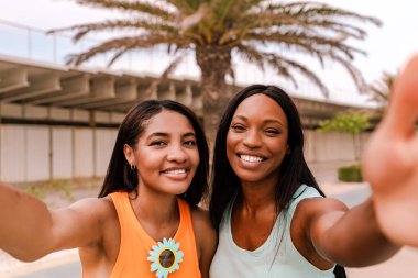 Güneşli bir günde palmiye ağacının altında selfie çeken iki çok ırklı arkadaş.