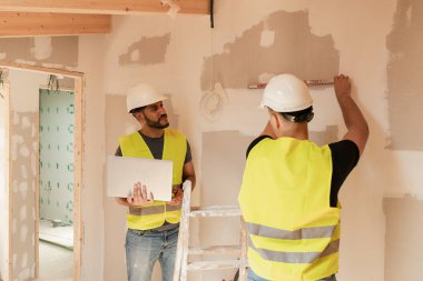 İki erkek inşaat işçisi duvarları yıkıyor ve tadilat sırasında dizüstü bilgisayar kullanıyor.