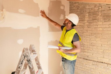 İnşaat işçisi duvara dokunarak inşaat alanındaki alçı işçiliğinin kalitesini kontrol ediyor.