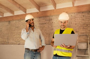 Evin yenilenmesi sırasında ustabaşı dizüstü bilgisayar kullanırken mimar telefonda konuşuyor.