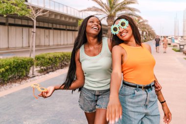 Komik güneş gözlüğü takan iki mutlu çok ırklı kadın gezinti güvertesinde yürüyor ve gülüyor.