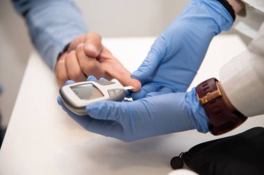 Eczanedeki hastaların kan şekeri seviyelerini ölçmek için glukometre kullanan mavi eldivenli eczacıya yaklaş.