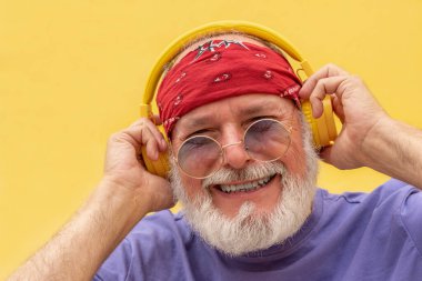 Bandana takan, kulaklık takan ve sarı arka planda gülümseyen mutlu son sınıf öğrencisi.