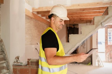 Güvenlik kaskı ve yelek giyen erkek inşaat işçisi dijital masa teftiş sahası kullanıyor.