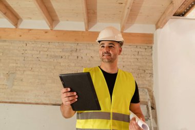 İnşaat sırasında elinde planlar tutarken dijital tablet kullanan Erkek Müteahhit