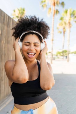 Kıvrımlı İspanyol sporcu dışarıda spor yaparken kablosuz kulaklıkla müzik dinliyor.